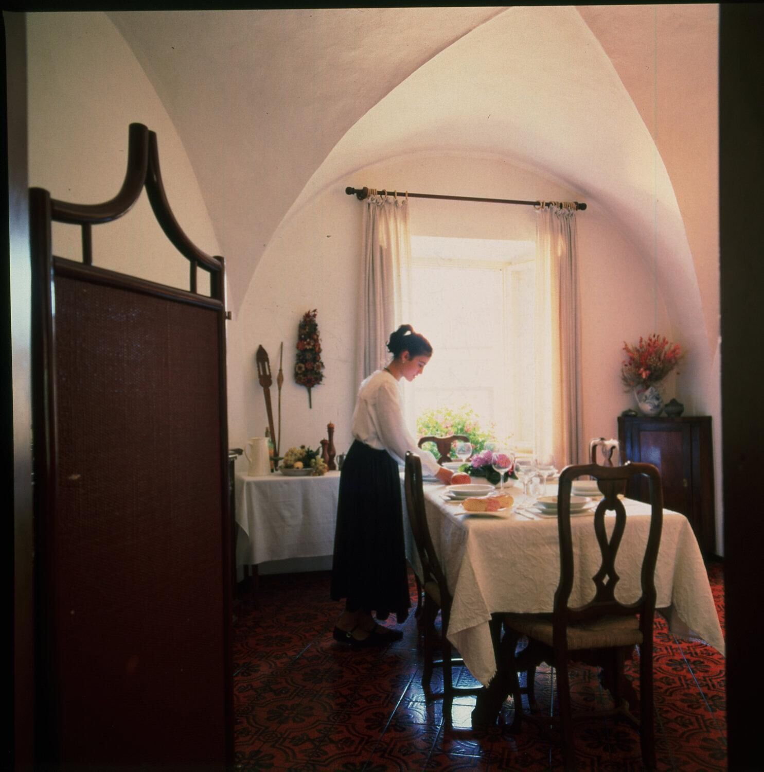 Una habitación con una mesa de comedor para dos personas, una ventana con cortinas y una puerta con marco de madera.