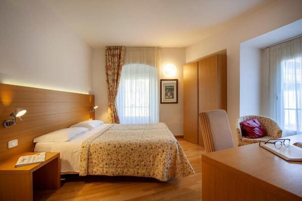 A hotel room with a bed, bedside table, chair, desk, and a window with curtains.