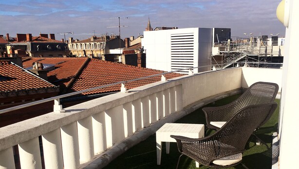 A balcony with a white railing, a small table, and two wicker chairs. - Ours Blanc-Wilson (Toulouse)