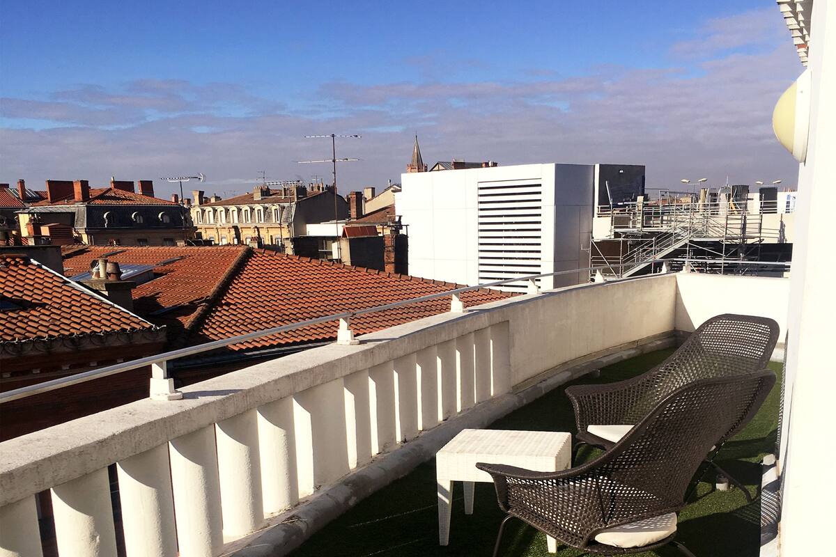 A balcony with a white railing, a small table, and two wicker chairs.