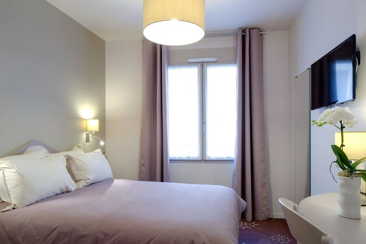 A hotel room with a bed, a desk, a TV, and a window with curtains.