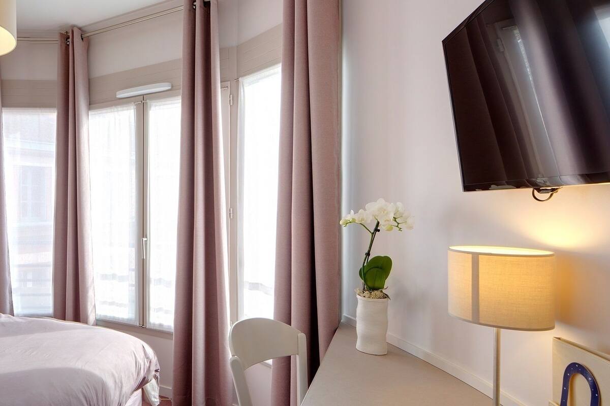 A hotel room with a bed, bedside lamps, a TV, and a window with curtains.
