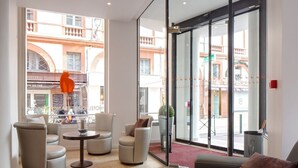 A modern hotel lobby with a seating area, large windows, and a view of the street. - Ours Blanc-Wilson (Toulouse)