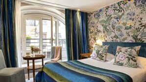 A hotel room with a bed, a chair, a small table, and a balcony with curtains. - Le Regent (Paris)
