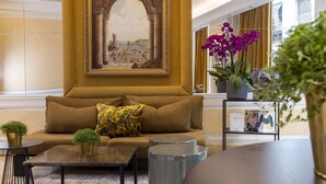 A lobby with a sofa, coffee table, and potted plants. - Le Regent (Paris)
