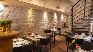 A restaurant with stone walls, a spiral staircase, and tables set for dining. - Le Regent (Paris)