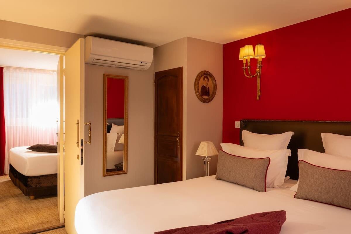 A hotel room with a large bed, a bedside table with a lamp, a mirror, and a red accent wall.