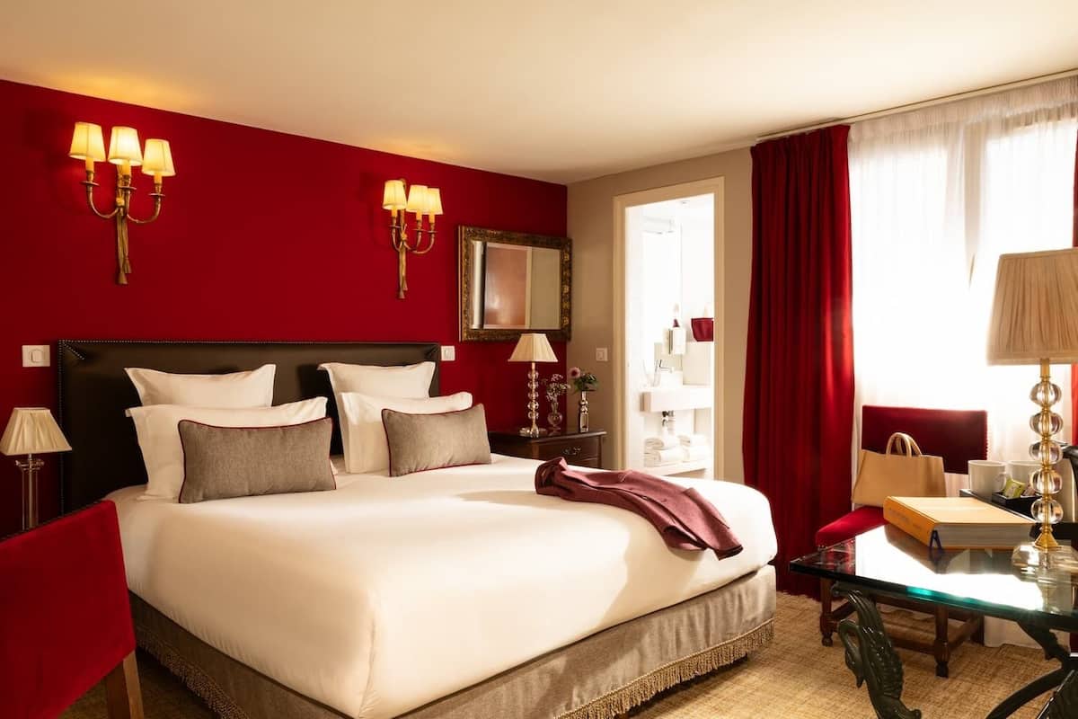 A hotel room with a large bed, a desk, a chair, a lamp, and a mirror.