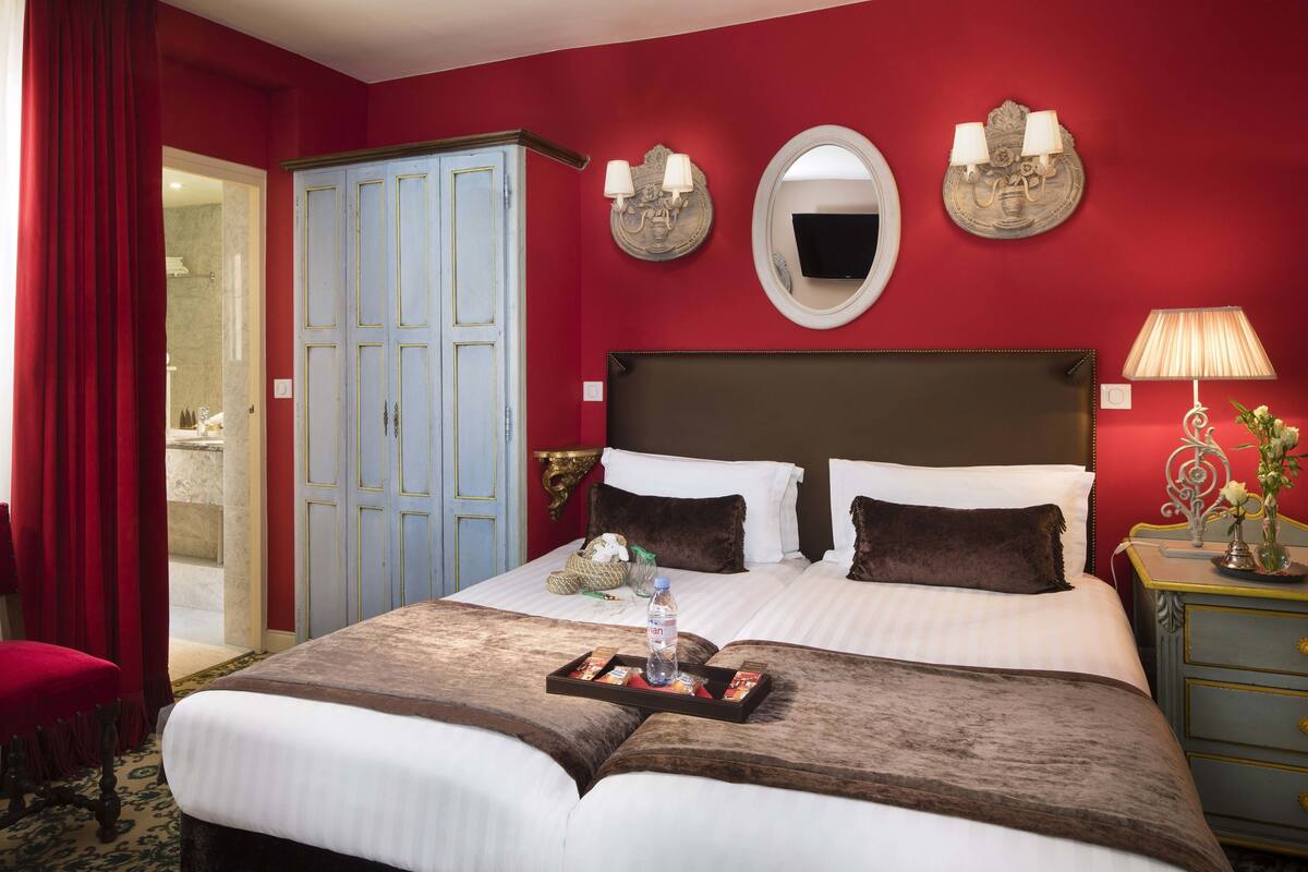 A hotel room with a large bed, a wardrobe, a mirror, and a bedside table with a lamp.