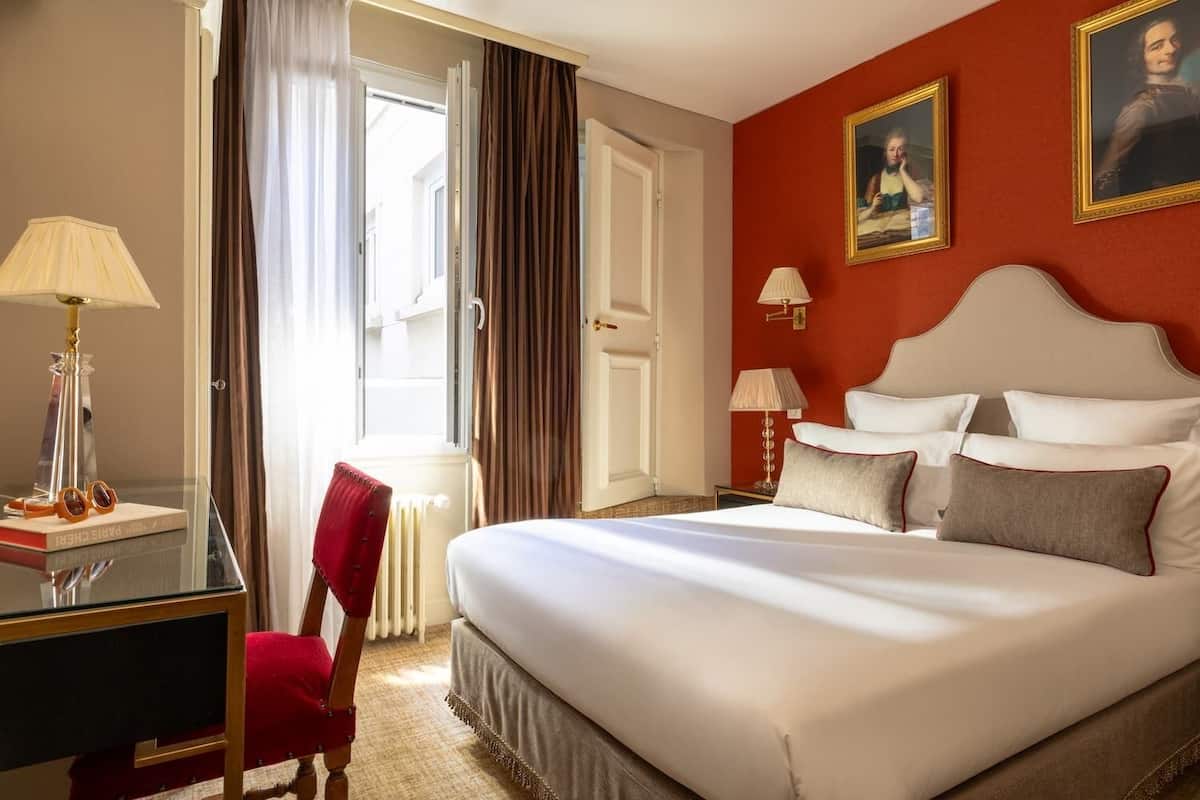 A hotel room with a bed, a desk, a chair, and two lamps.