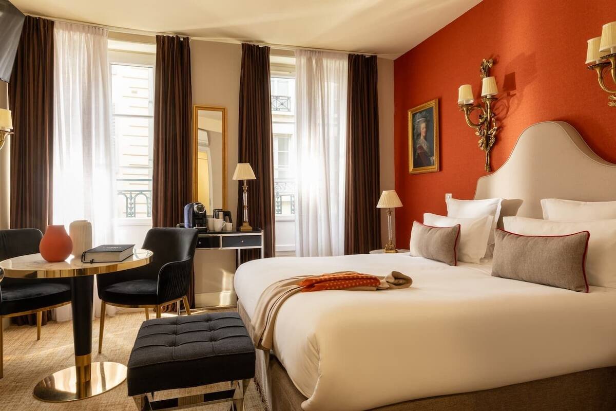 A hotel room with a large bed, a desk, a chair, a round table, and a window with curtains.