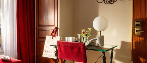 A room with a wooden door, a red chair, a glass table with a book, a vase with flowers, and a lamp.