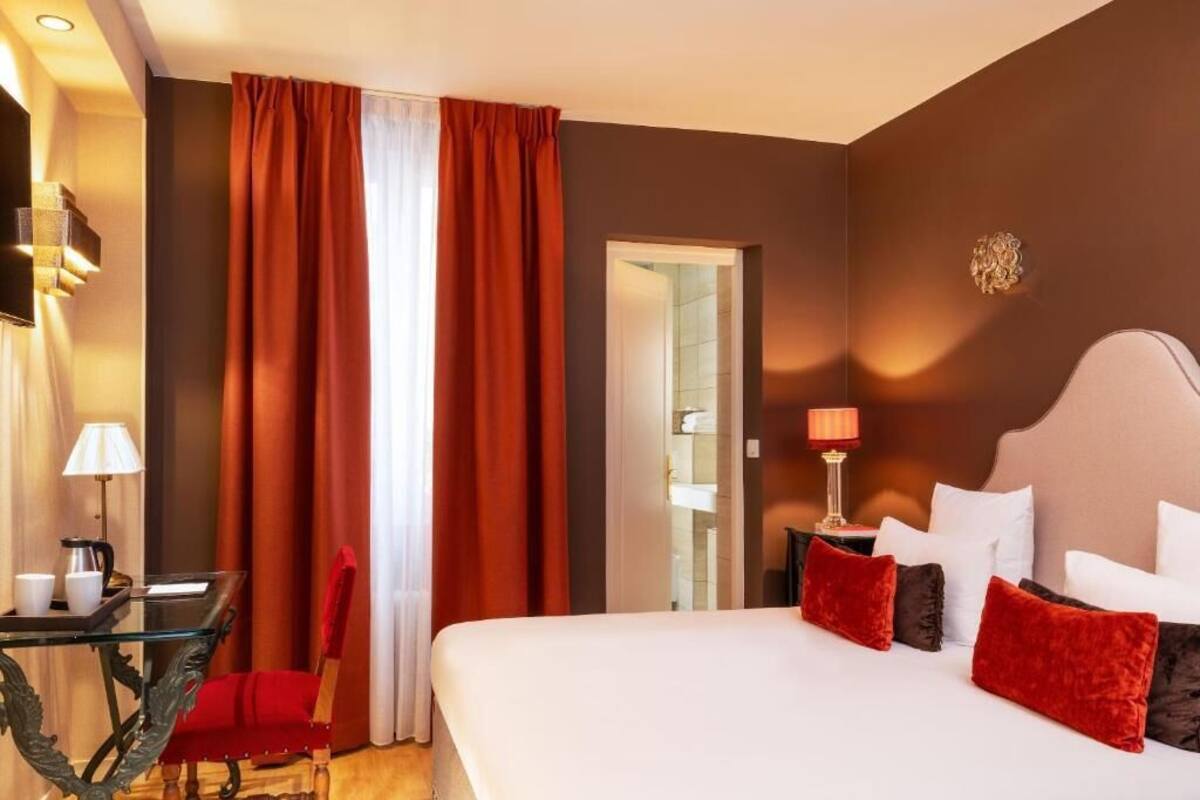 A hotel room with a large bed, a desk with a lamp, and a chair.