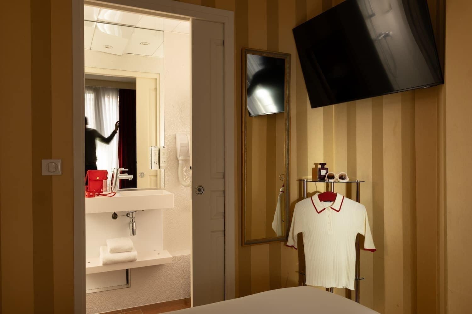 Ein Hotelzimmer mit Bett, Wand-Fernseher, Spiegel, Waschbecken und Kleiderständer.