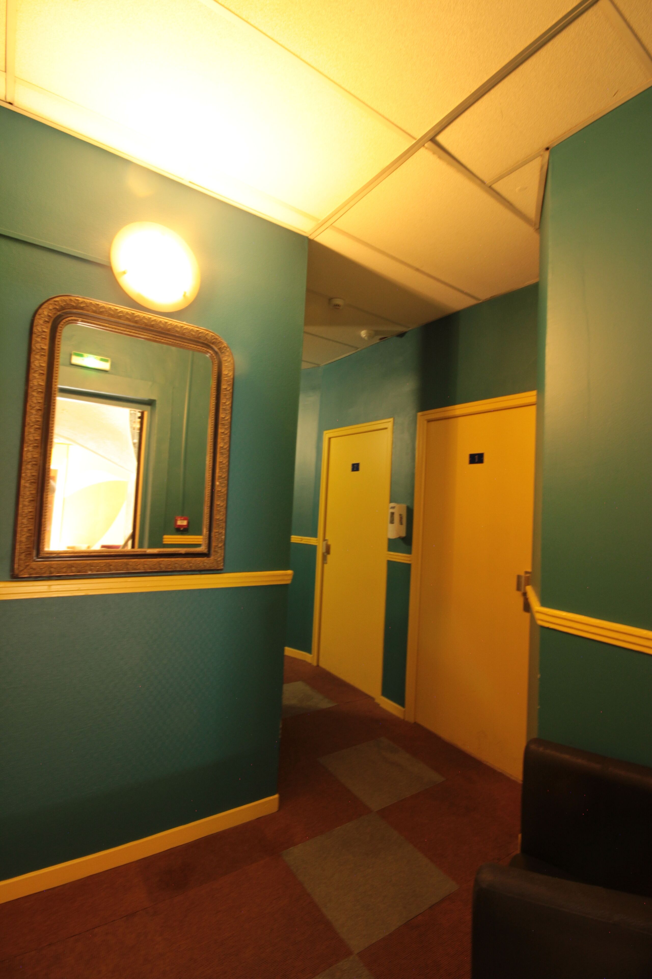 A hallway with teal walls, a mirror, and doors.