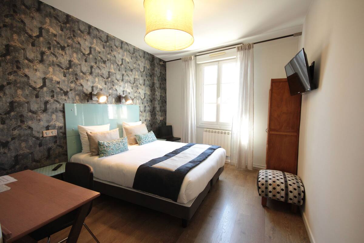 Habitación de hotel con cama, escritorio, silla, televisor y ventana con cortinas.