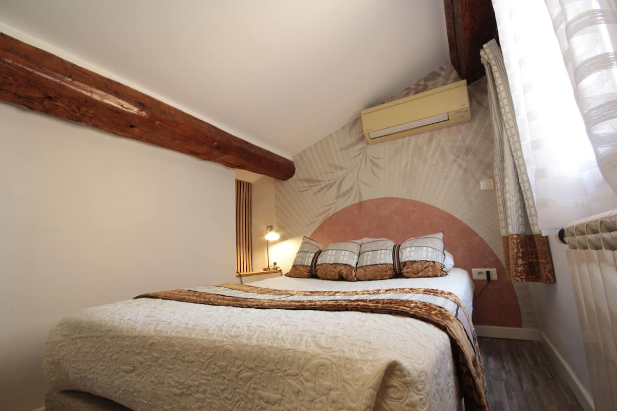 Un dormitorio con cama, mesita de noche, lámpara y aire acondicionado.