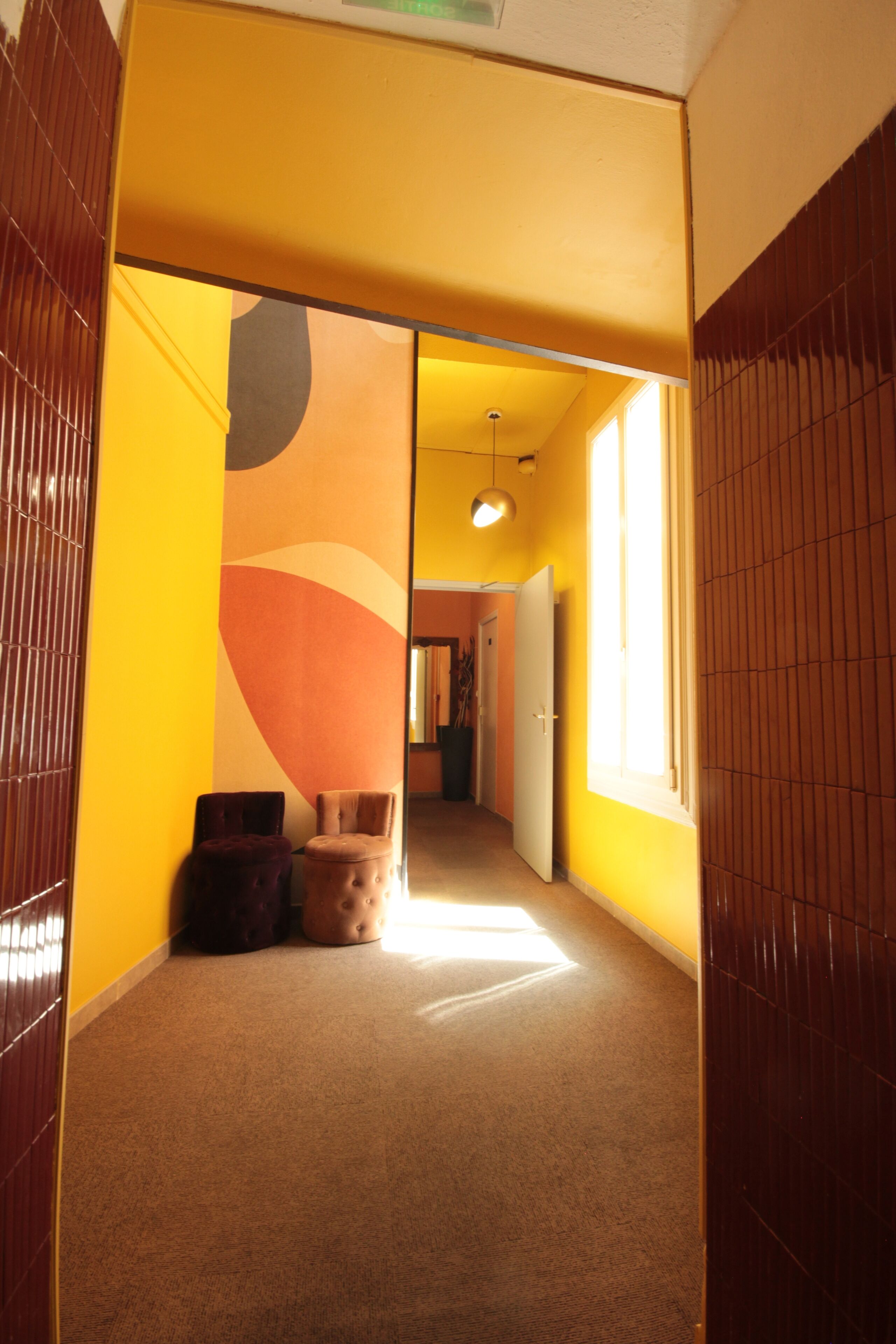 A hallway with a yellow wall, a brown floor, and a door leading to another room.