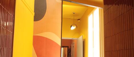 A hallway with a yellow wall, a brown floor, and a door leading to another room.