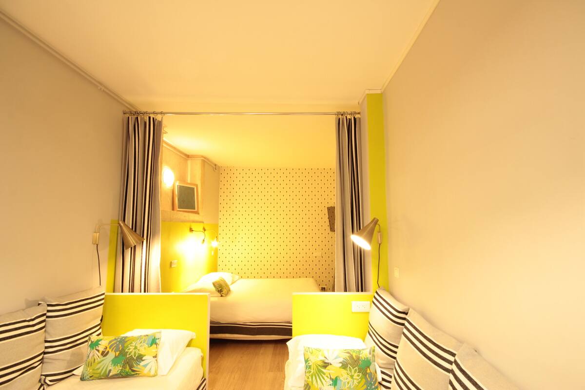 Una habitación pequeña e iluminada con una cama, dos mesitas de noche y un buró.
