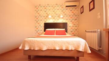 A bedroom with a bed, floral wallpaper, two wall-mounted lights, an air conditioner, and a radiator.