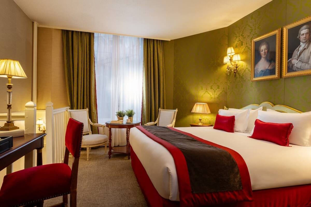 Une chambre d’hôtel avec un grand lit, deux chaises, un bureau et une petite table avec une lampe.