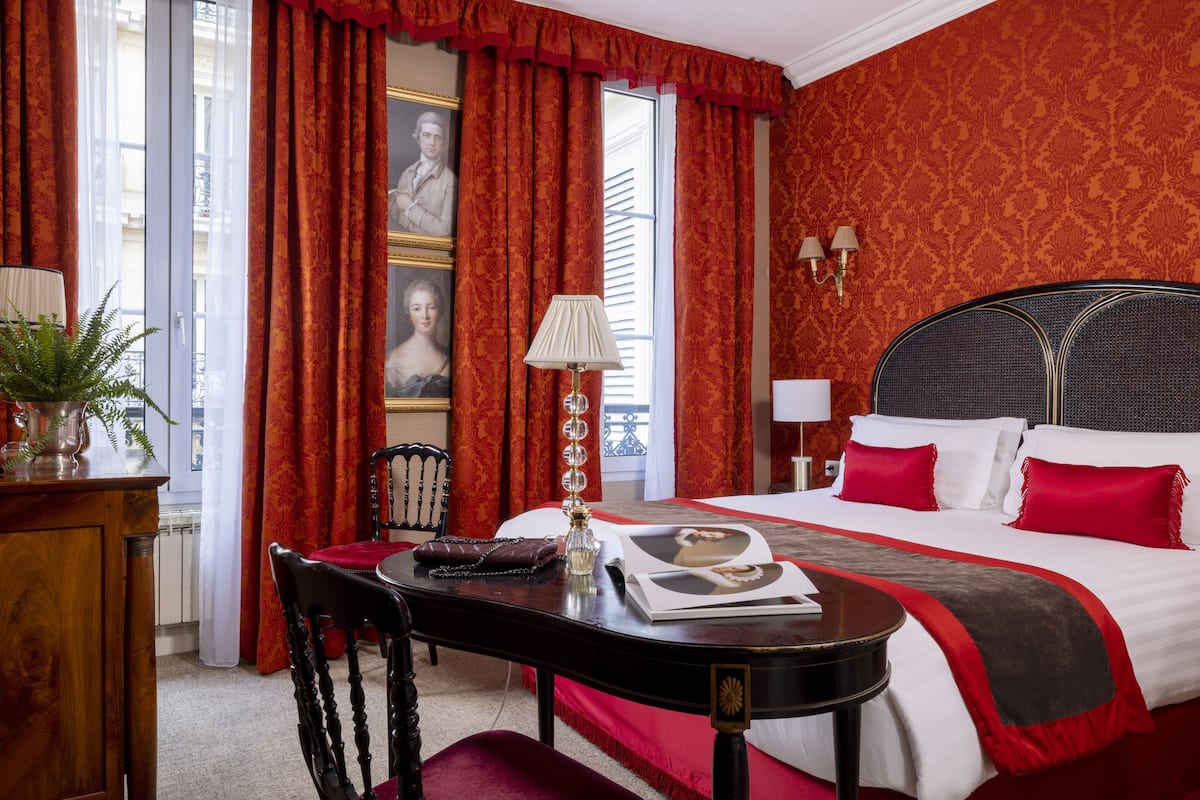 Une chambre d’hôtel avec un grand lit, des rideaux rouges, un bureau avec une lampe et une chaise.