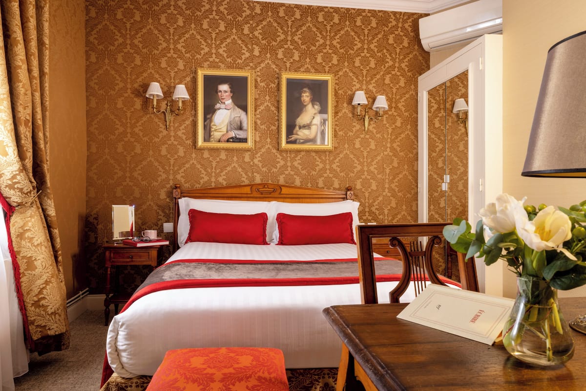 Une chambre d’hôtel avec un lit, une table de chevet, un miroir, un bureau et un vase avec des fleurs.