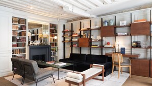 A modern living room with a fireplace, bookshelves, a black sofa, and a wooden coffee table. - Hotel Verneuil (Paris)