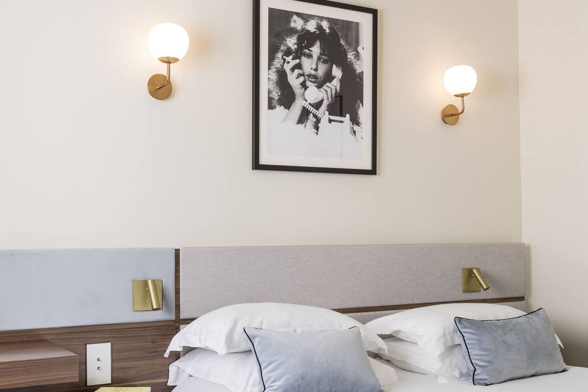 A modern hotel room with a neatly made bed, a bedside table with a lamp, and a framed picture on the wall.