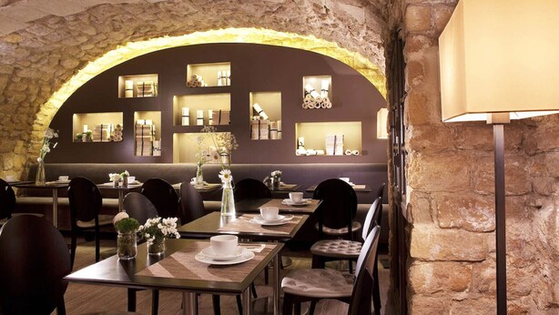 A restaurant with stone arches, wooden tables, and chairs. There are shelves with bottles and glasses on the walls. - Hotel Verneuil (Paris)