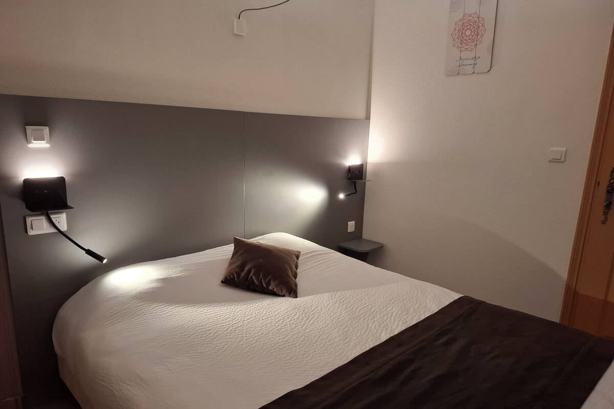 Ein ordentlich bezogenes Bett mit weißer und brauner Bettdecke, zwei Nachttischlampen und einer an der Wand montierten Steckdose.