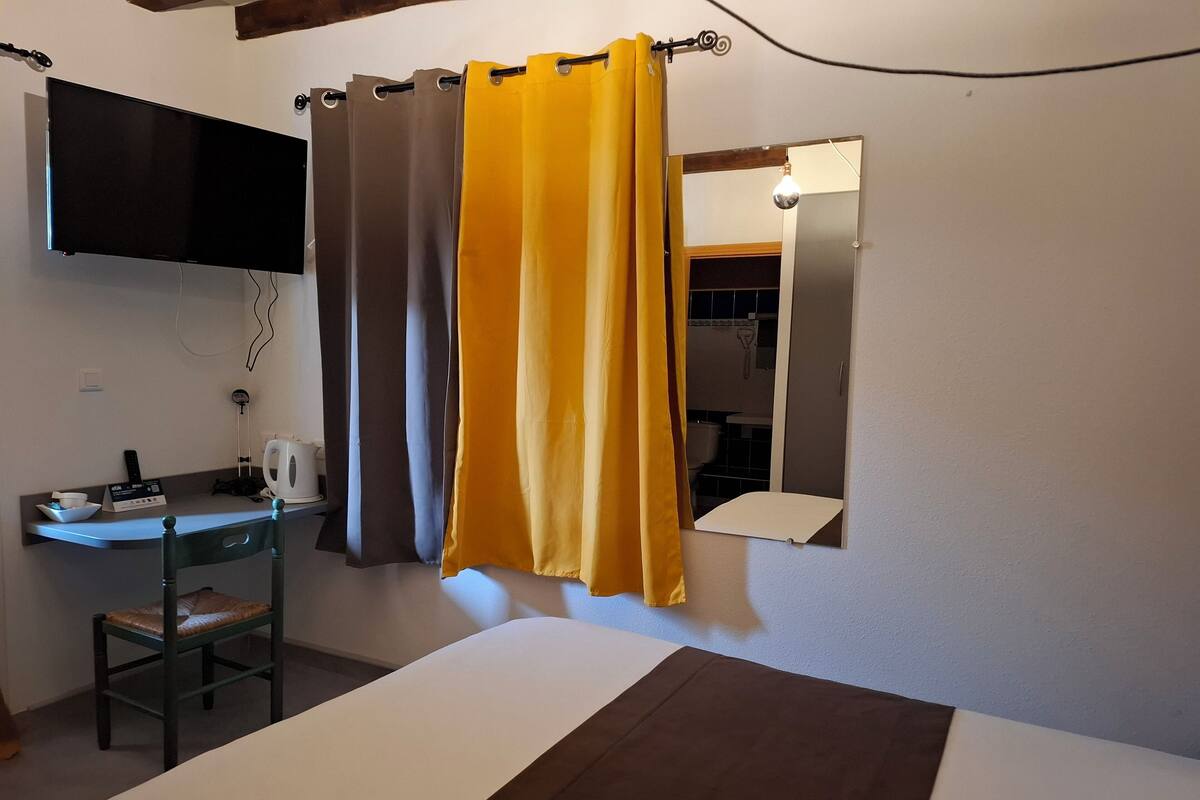 Ein Hotelzimmer mit einem Bett, einem Schreibtisch mit Stuhl, einem an der Wand montierten Fernseher und einem durchgegangene Tür sichtbaren Badezimmer.