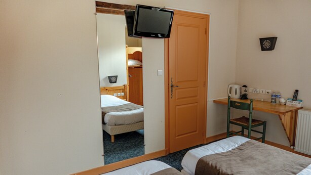 Habitación de hotel con dos camas, un escritorio con silla, un televisor montado en la pared y una puerta que da a otra habitación.