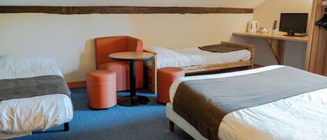 A room with two beds, a small table, a chair, and a TV on a shelf.