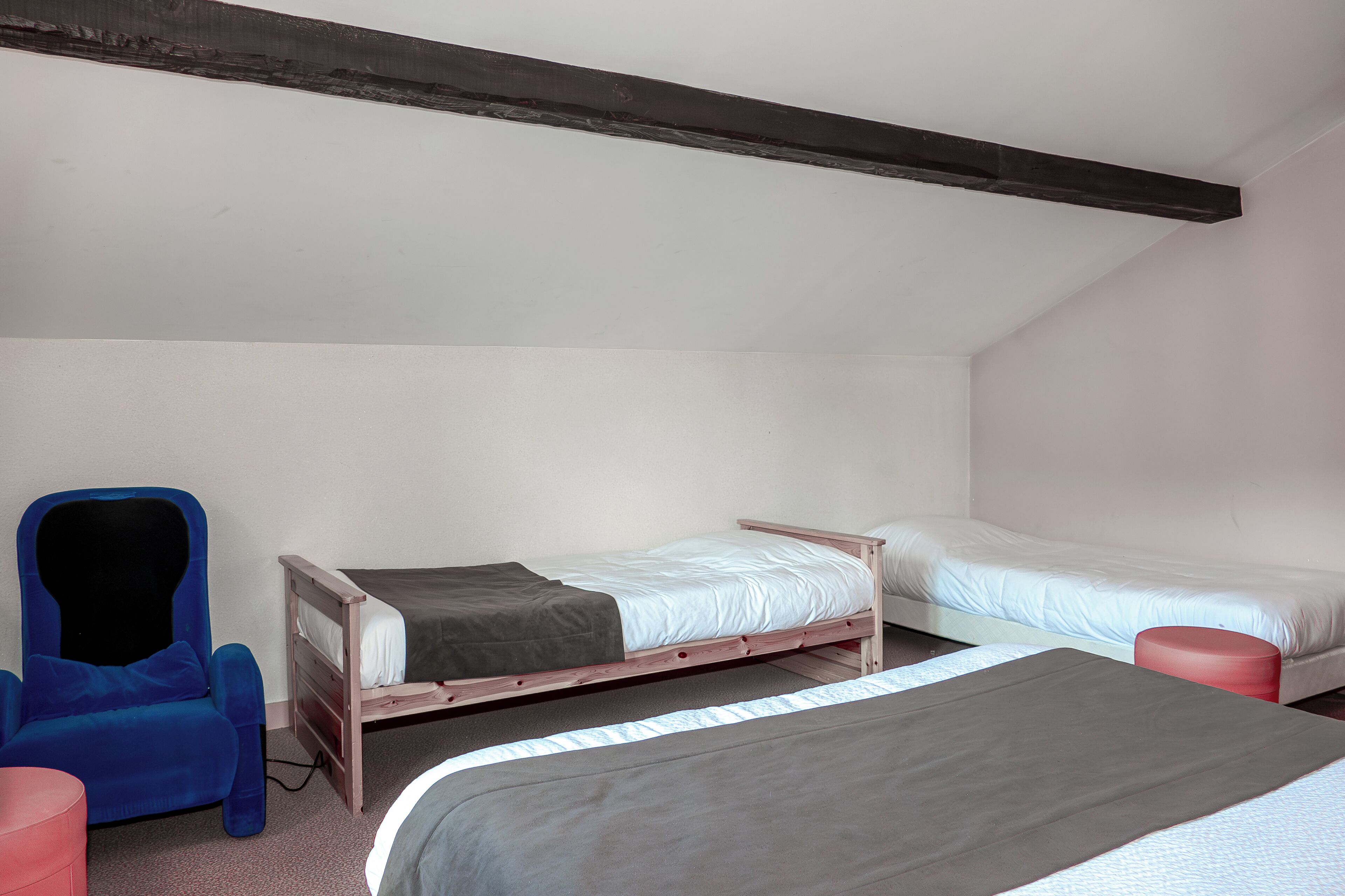 A bedroom with two single beds, a blue chair, and a red stool.