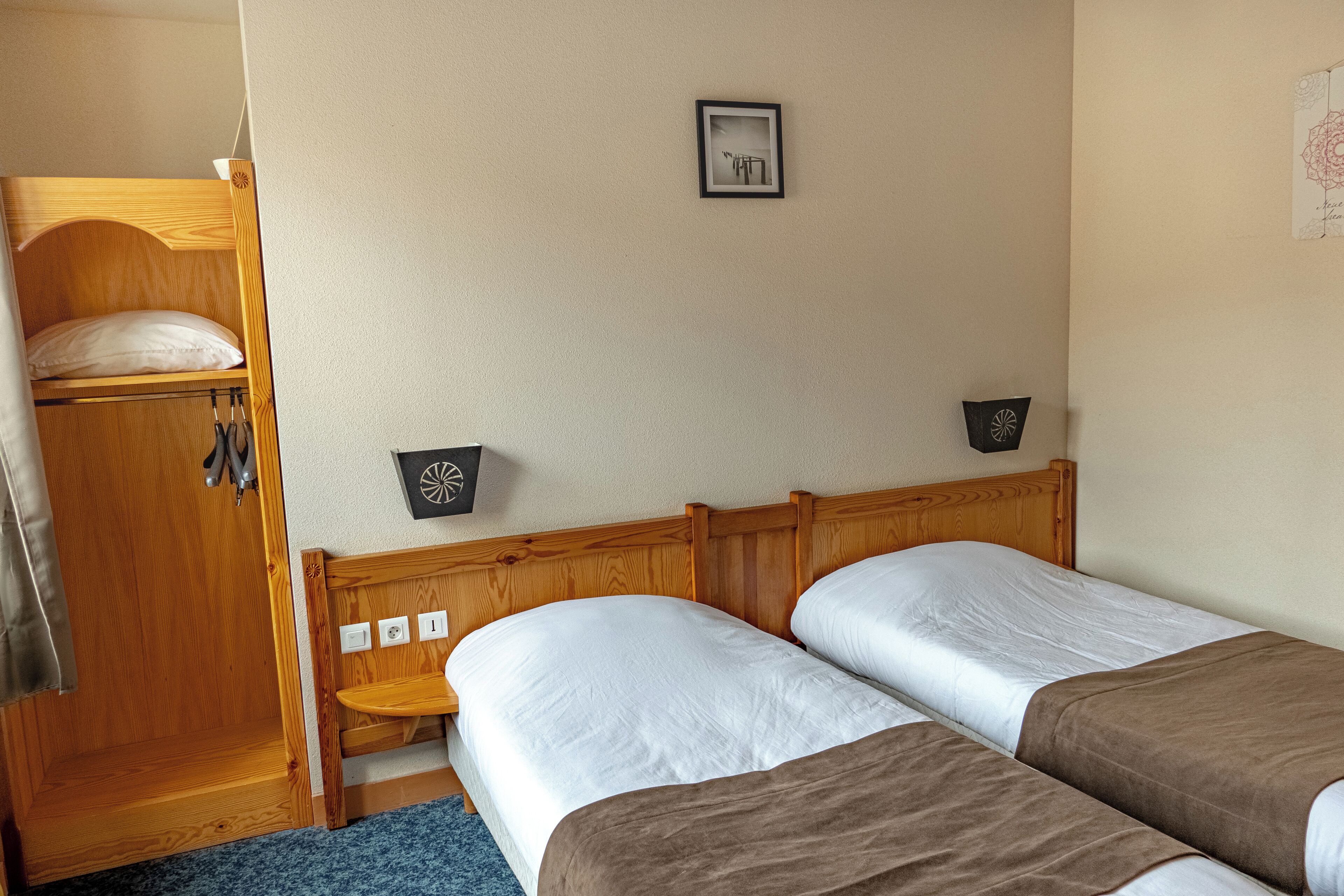 A bedroom with two single beds, a wooden wardrobe, and a small table.