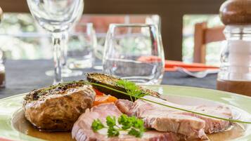 A plate with sliced meat, vegetables, and a garnish on a table with glasses and a salt shaker in the background.