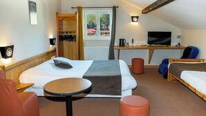 Habitación de hotel con cama, escritorio con computadora, silla, una mesita y ventana con cortinas.