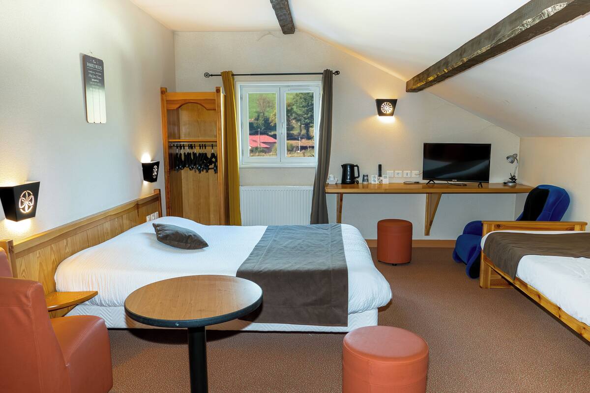 Ein Hotelzimmer mit einem Bett, einem Schreibtisch mit Computer, einem Stuhl, einem kleinen Tisch und einem Fenster mit Vorhängen.