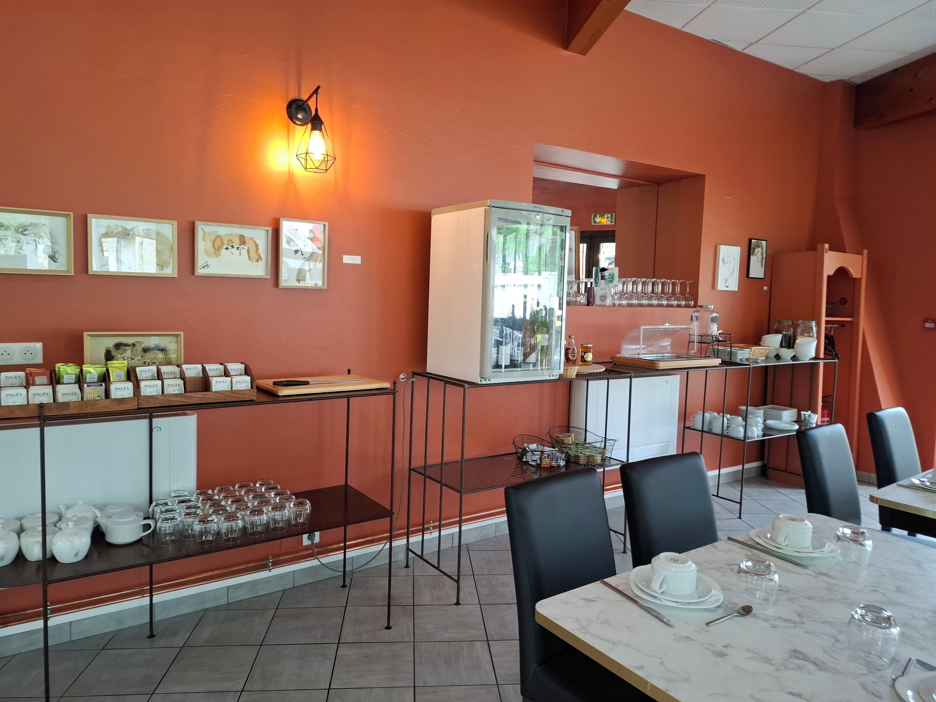 A restaurant interior with a red wall, framed artwork, a coffee station, and a counter with glassware.