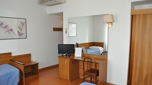 Une chambre d’hôtel comprenant un lit, un bureau avec un ordinateur, une chaise, une petite table, un miroir et une lampe fixée au mur.