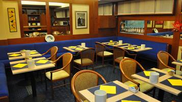 Un ristorante con sedute blu e tavoli di legno, ognuno con un sottopiatti giallo e un portatovaglioli bianco.