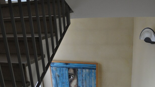 Un escalier avec une rampe en bois, un tableau encadré de bleu accroché au mur et une fenêtre avec des stores.