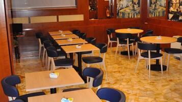 A restaurant with multiple tables and chairs, a tiled floor, and paintings on the walls.