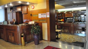 Un hall d’hôtel comprenant un comptoir d’accueil, une horloge, un panneau « interdiction de fumer », un bar et une poubelle.