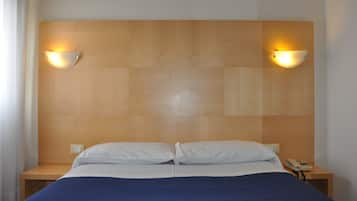 Habitación de hotel con cabecera de madera, dos lámparas de noche, cama con ropa de cama blanca y azul, y teléfono en la mesita de noche.