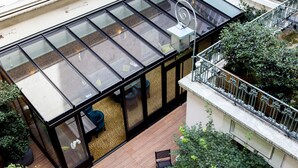 A modern glass-enclosed room with a wooden deck, a spiral staircase, and a view of the surrounding greenery. - Hotel Concortel (Paris)