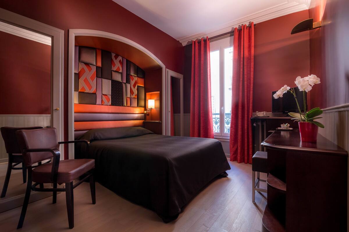 Ein Hotelzimmer mit Bett, Schreibtisch, Stuhl, Fernseher und einer Topfpflanze.