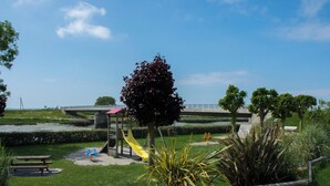 A playground with a slide and swings, a picnic table, and a bridge in the background. - Hôtel Rose (Beauvoir)